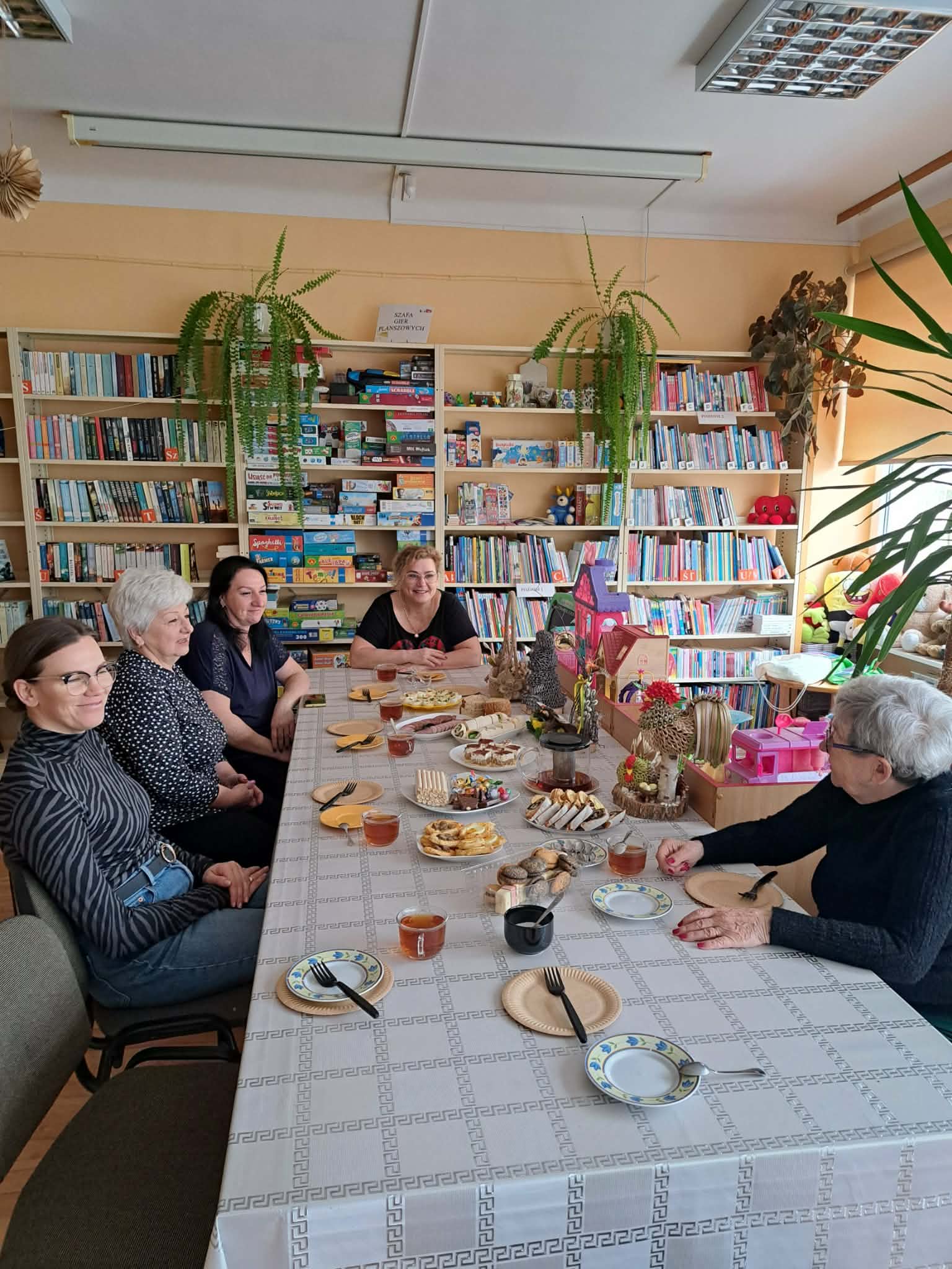 Panie siedzą przy wspólnym stole, zastawionym wielkanocnymi potrawami.