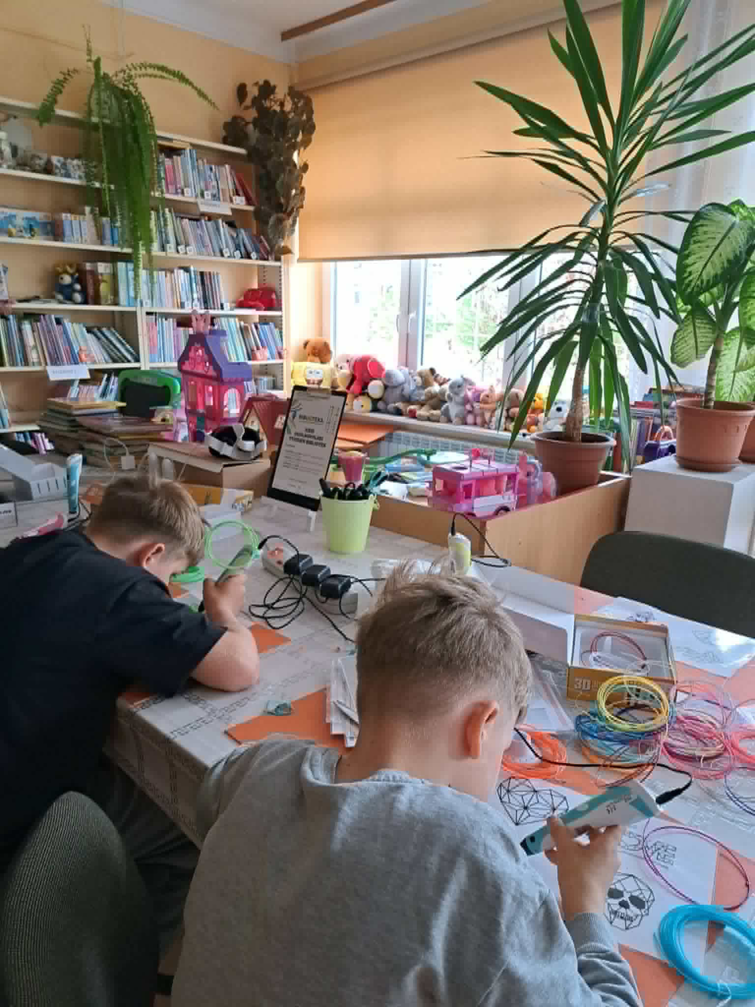 Dwaj chłopcy siedzą przy stole i pracują z długopisami 3D