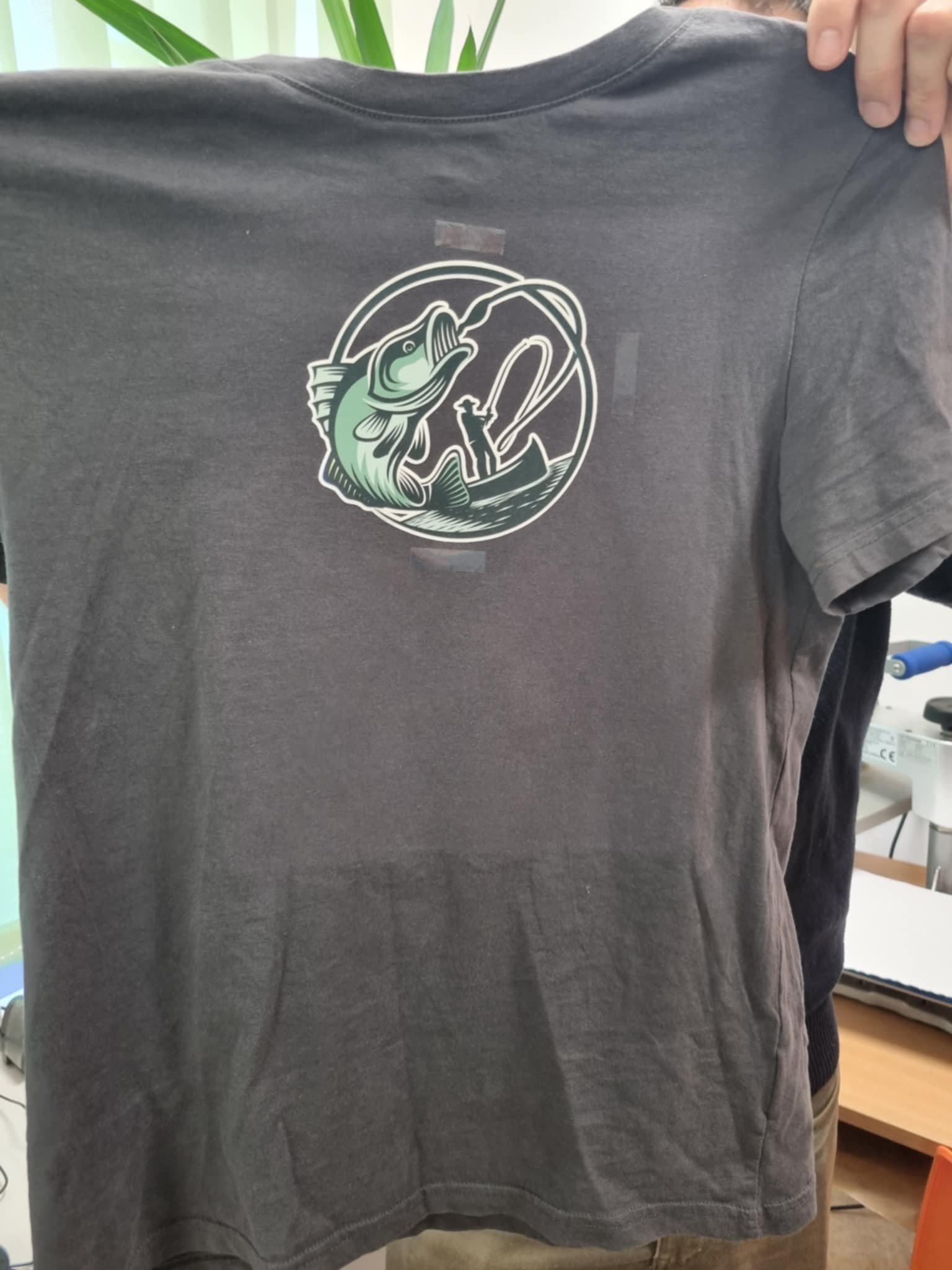 zdjęcie rąk trzymających koszulkę z nadrukiem rybaka i ryby