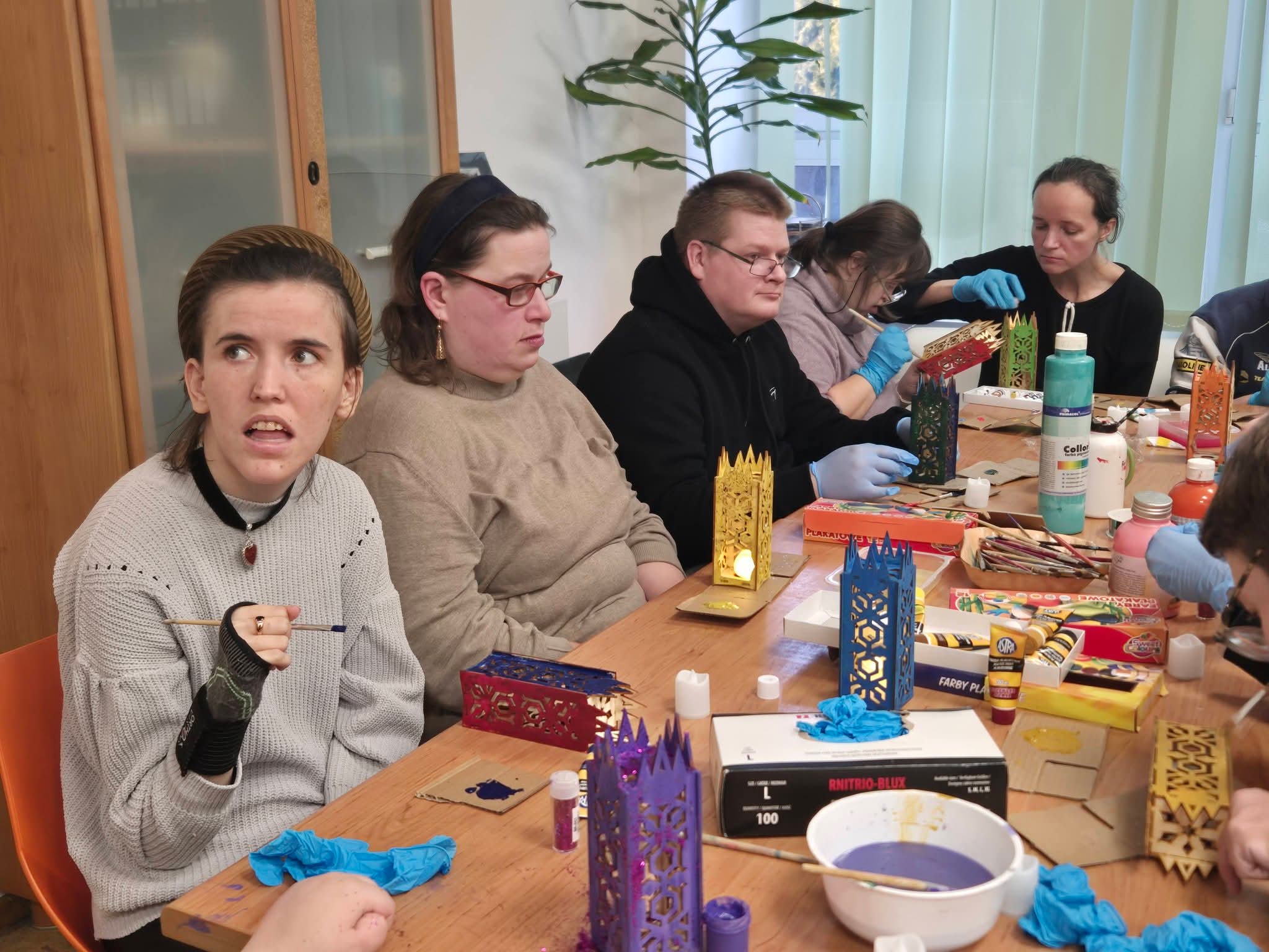 Grupa osób siedzi przy stole i maluje lampiony.