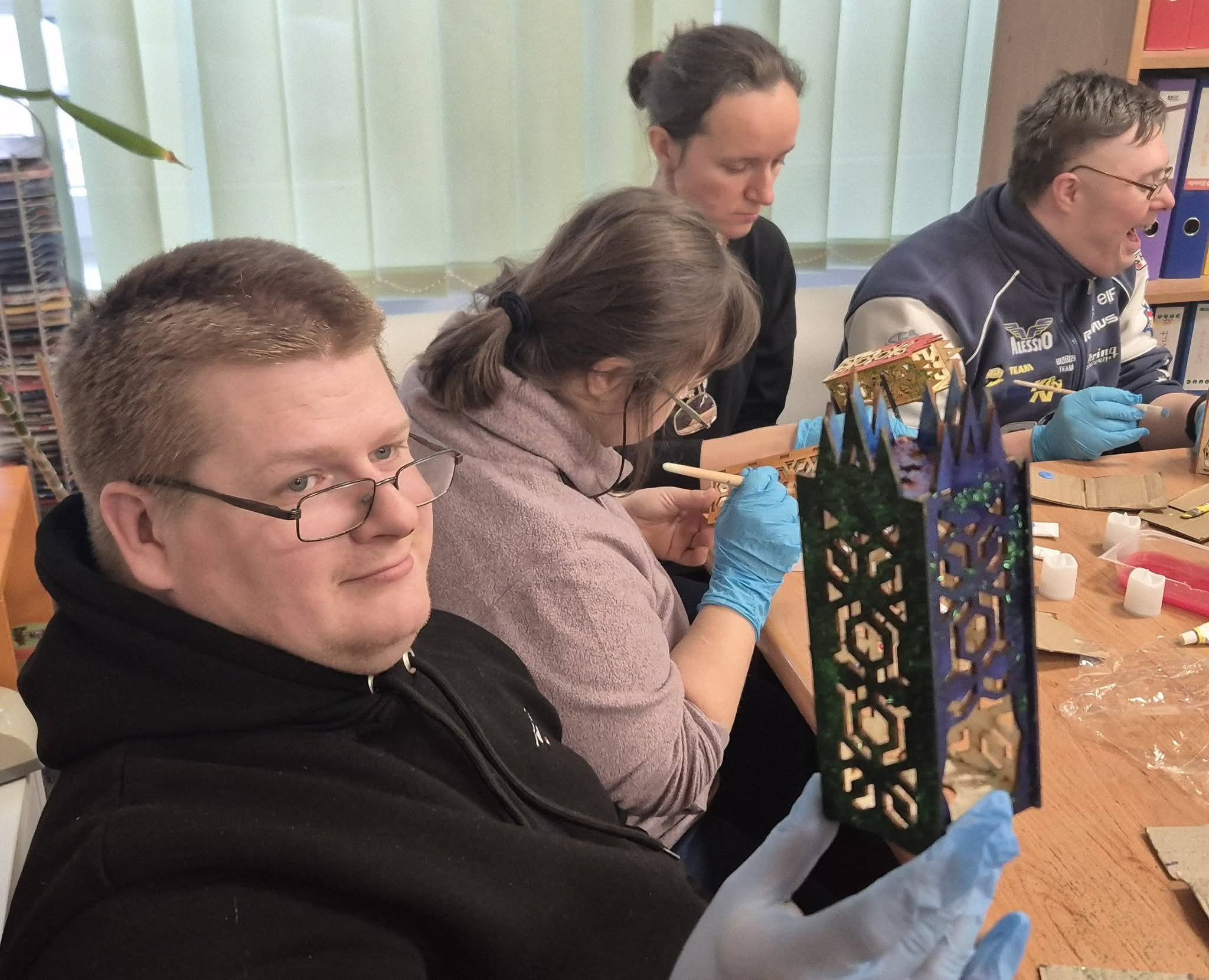 Grupa osób siedzi przy stole i maluje lampiony.