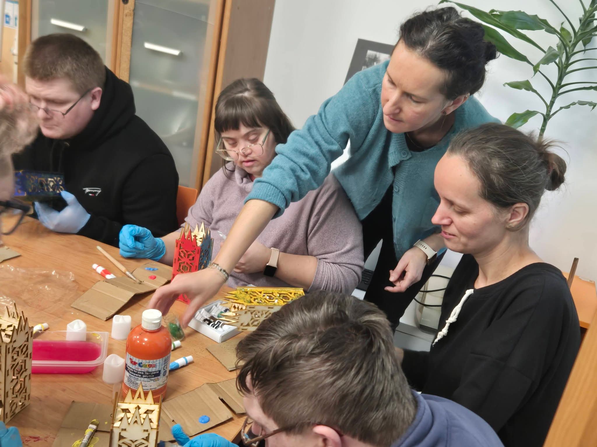 Grupa osób siedzi przy stole i maluje lampiony.