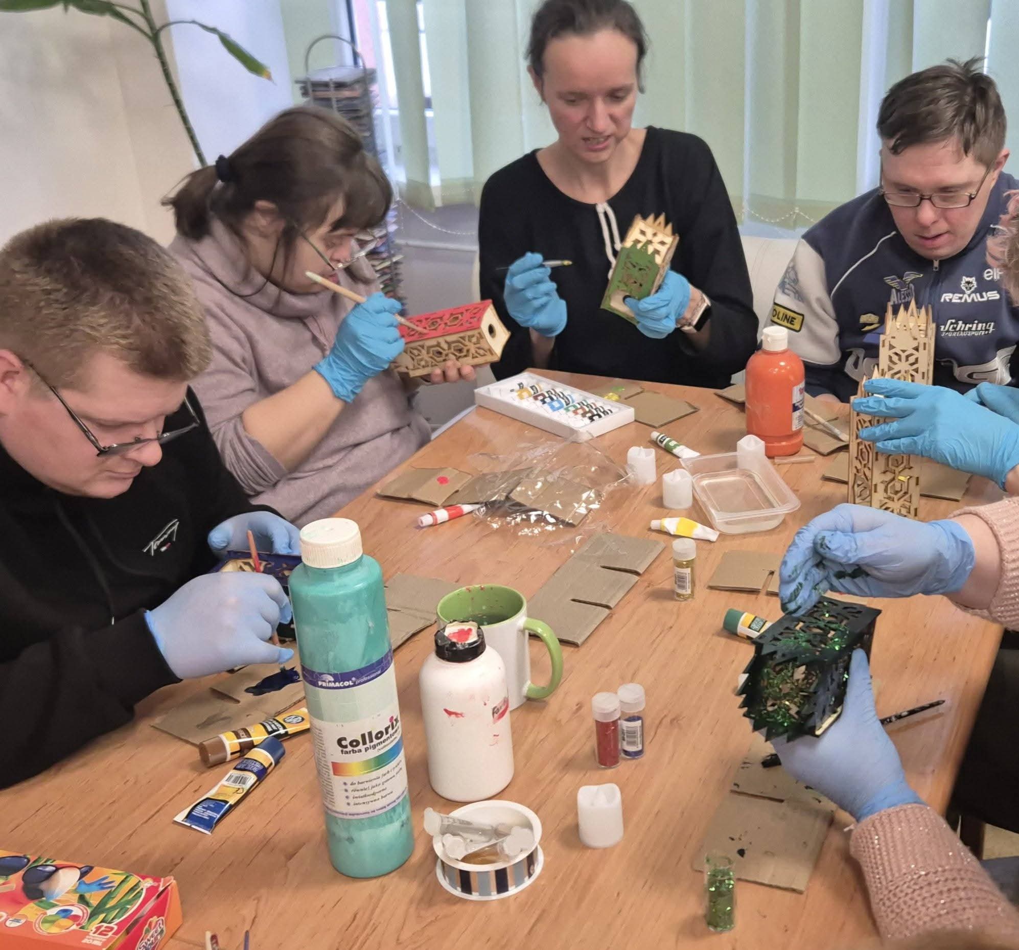 Grupa osób siedzi przy stole i maluje lampiony.