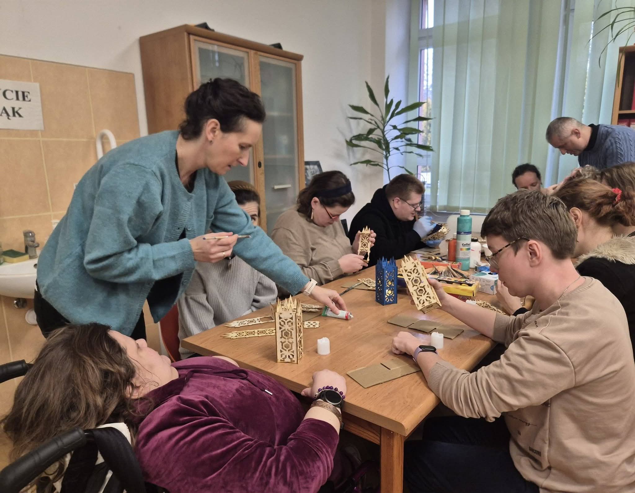 Grupa osób siedzi przy stole i maluje lampiony.