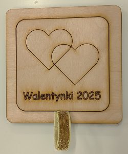 Drewniana tabliczka ze wstążką, na tabliczce zarys dwóch serc i napis: "Walentynki 2025"