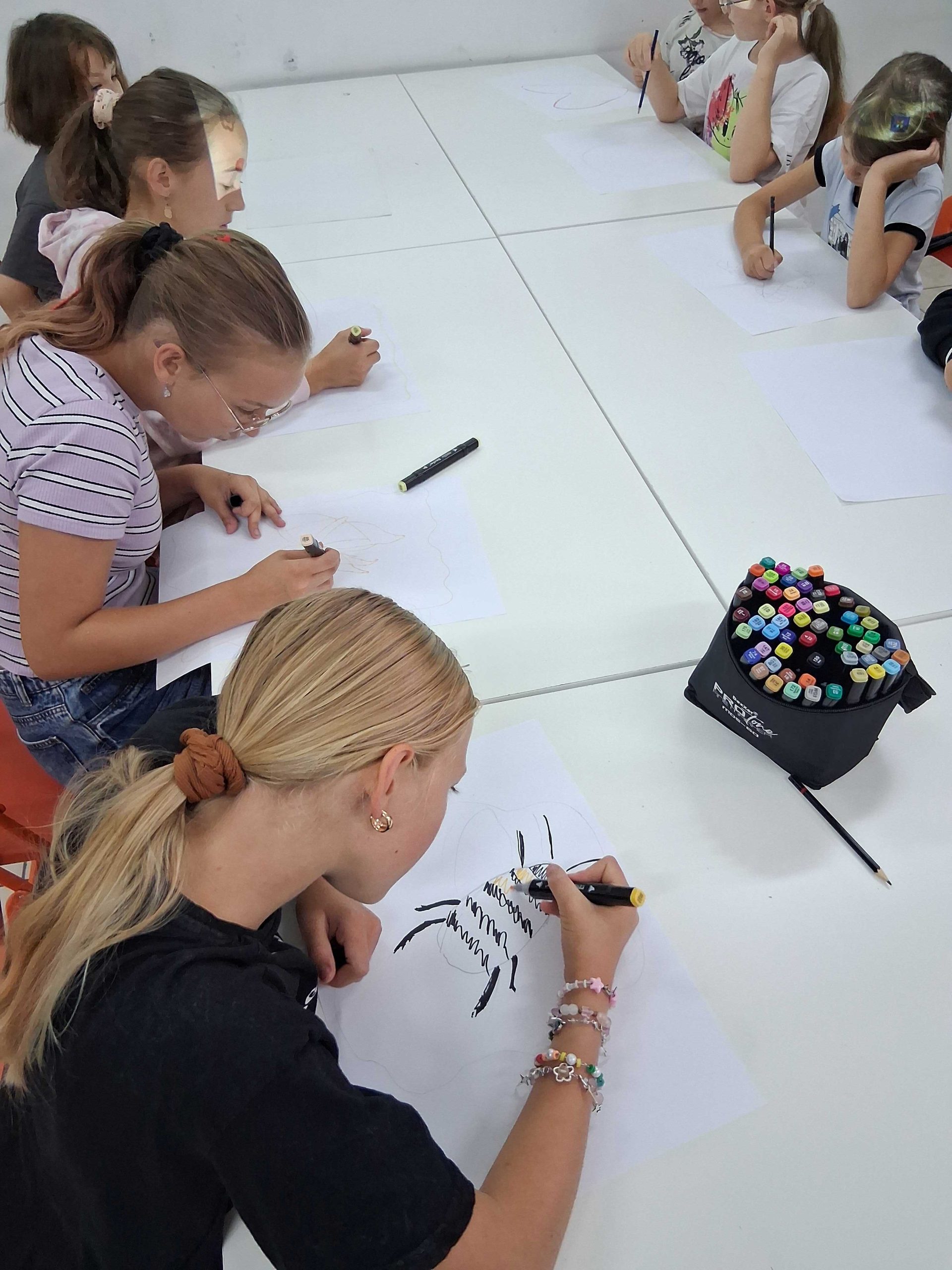 Zdjęcie dzieci przy biurkach, rysujących na kartkach papieru projekty prac