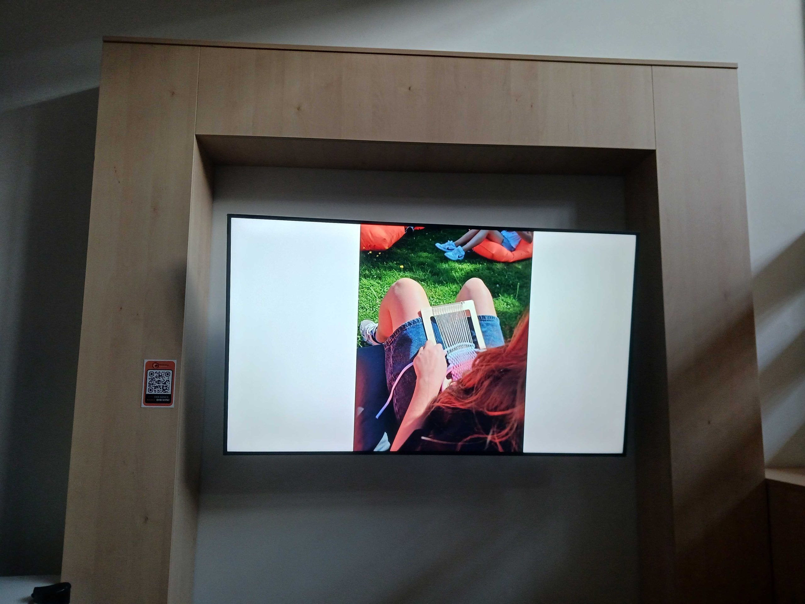 Zdjęcie ekranu, na którym wyświetla się zdjęcie siedzącego na pufie dziecka które tka.