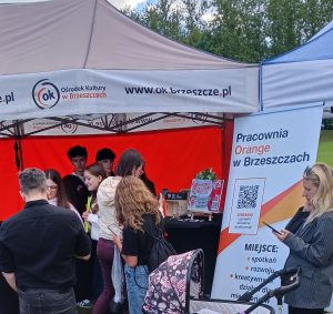 Na zdjęciu widać kilka osób skupionych przy stoisku plenerowym Pracowni Orange, pod namiotem, podczas wydarzenia Etno Skarby Brzeszcz.