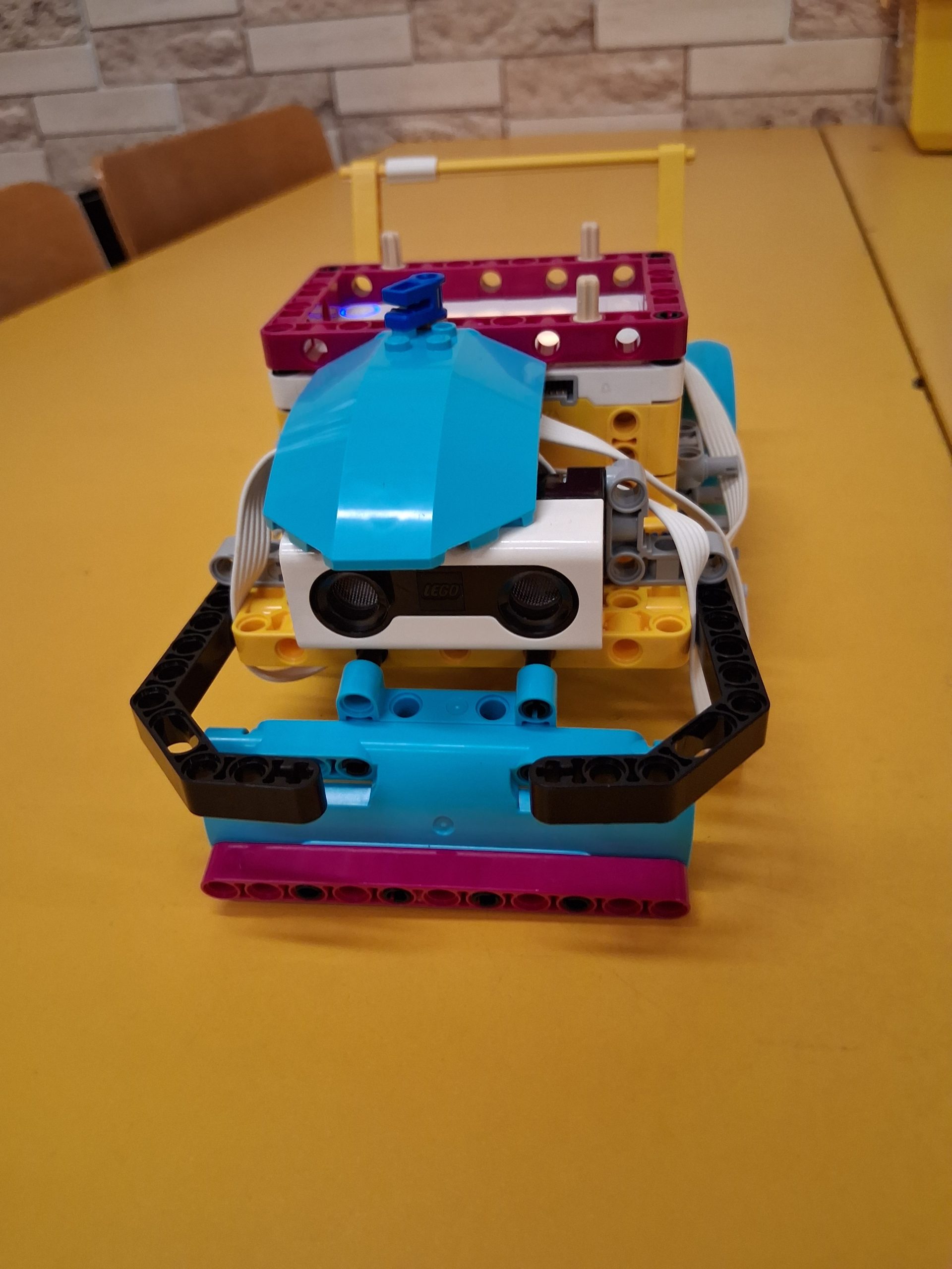 Robot/pojazd zbudowany z kolorowych klocków lego, leżący na żółtym stoliku.