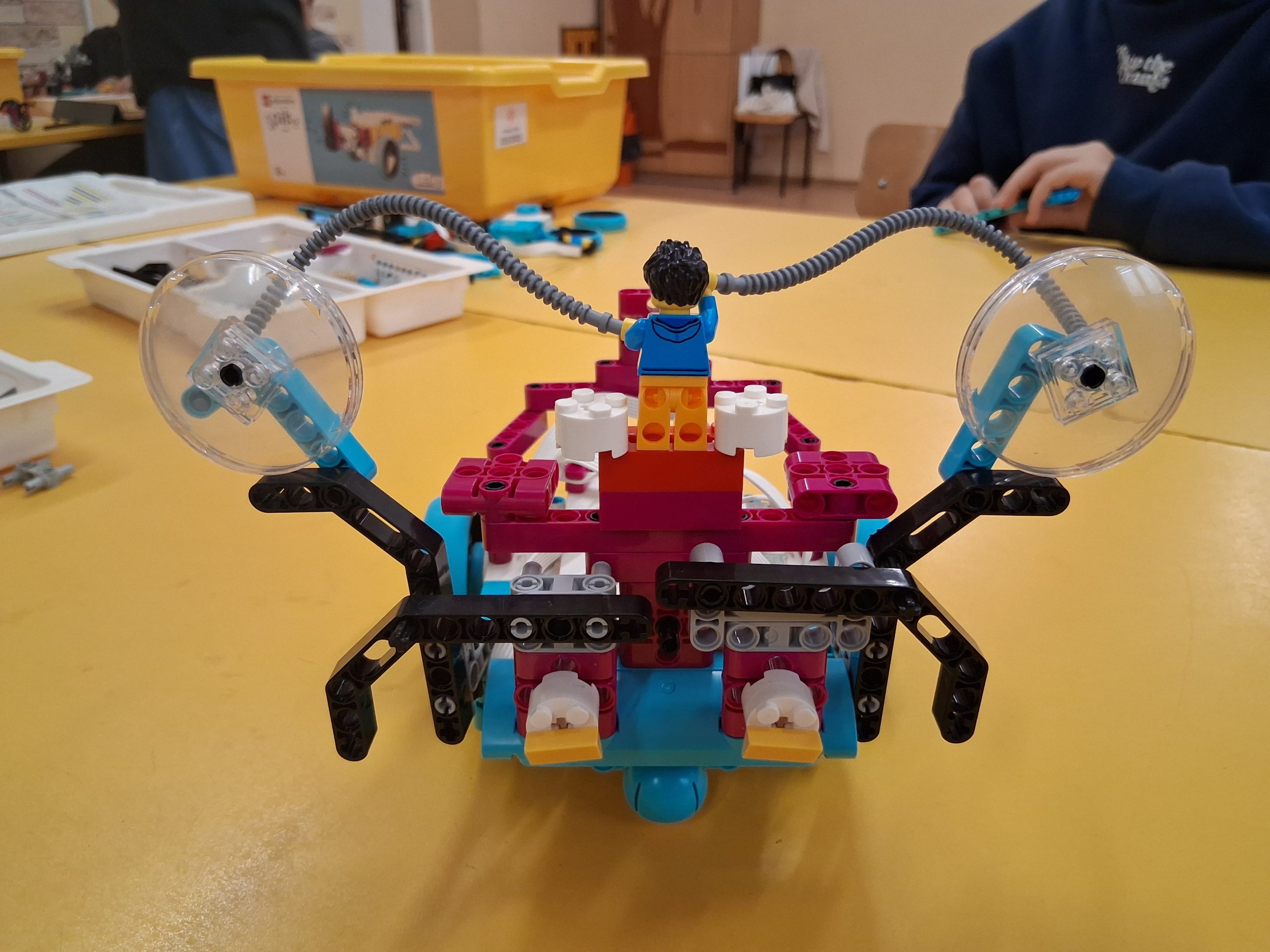 Robot/pojazd zbudowany z kolorowych klocków lego, leżący na żółtym stoliku.