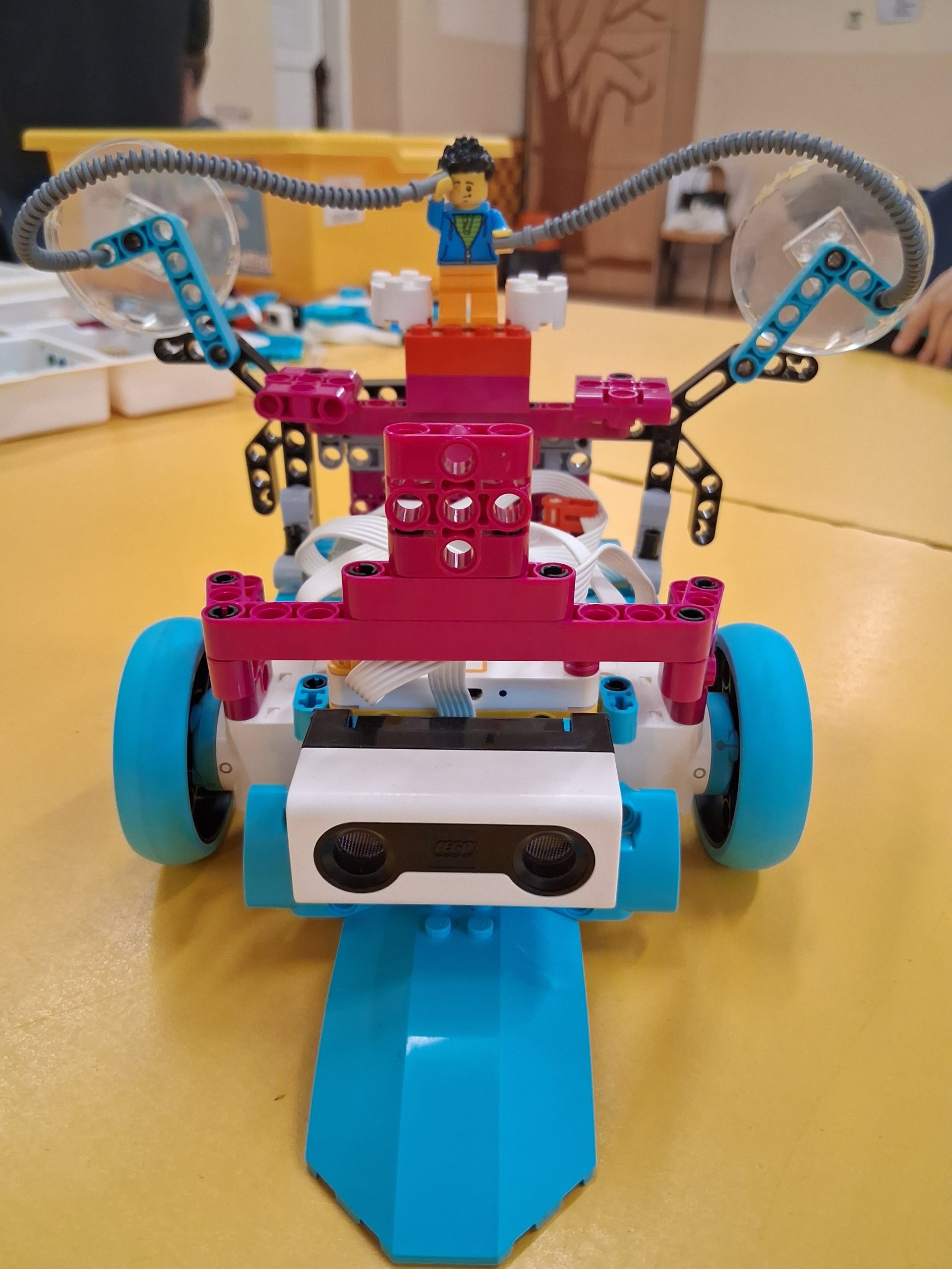 Robot/pojazd zbudowany z kolorowych klocków lego, leżący na żółtym stoliku.