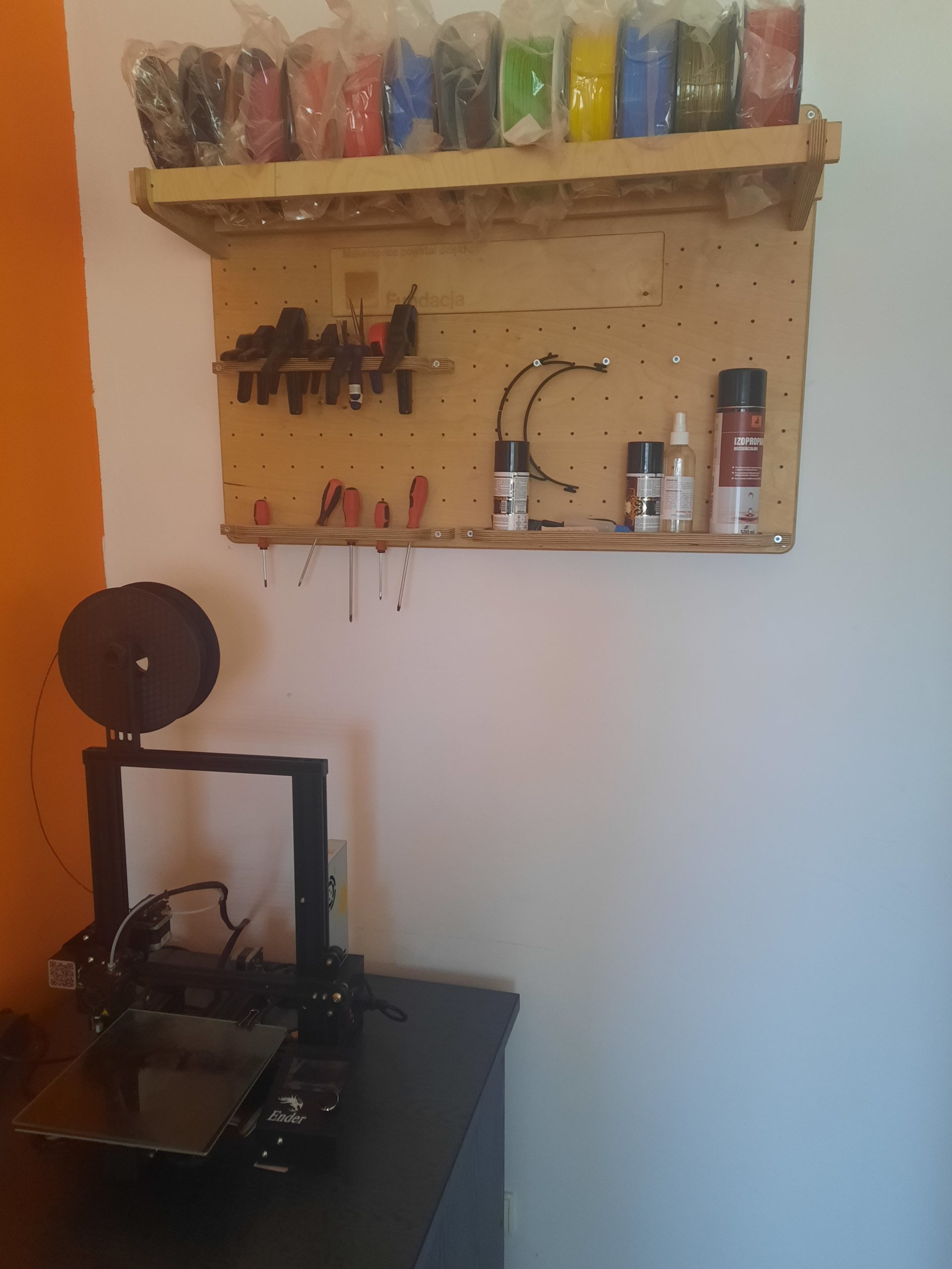 zdjęcie drukarki 3d nad którą wisi tablica z akcesoriami do drukarki