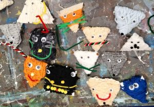 Na stole leżą prace plastyczne wykonane przez dzieci z włóczki, to kolorowe - trójkątne i kwadratowe - buźki, które mają oczy i wąsy.