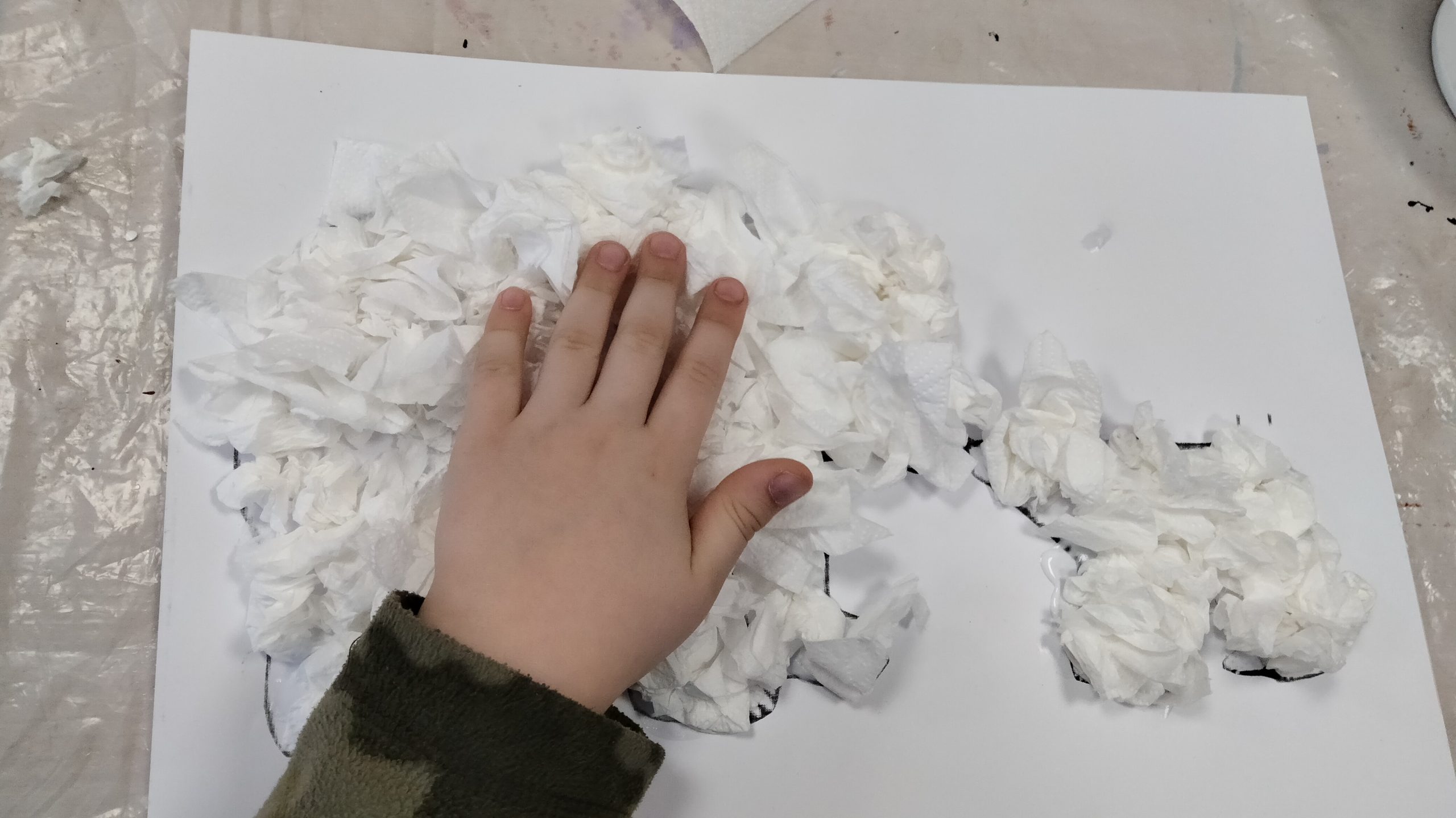 Na zdjęciu widać pracę plastyczną - kształty wyklejone białym papierem toaletowym. Tej faktury dotyka dziecięca ręka.