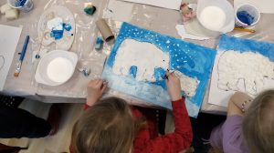 Na zdjęciu widać dziecko tworzące obrazek przedstawiający dwa niedźwiedzie polarne na niebieskim tle.