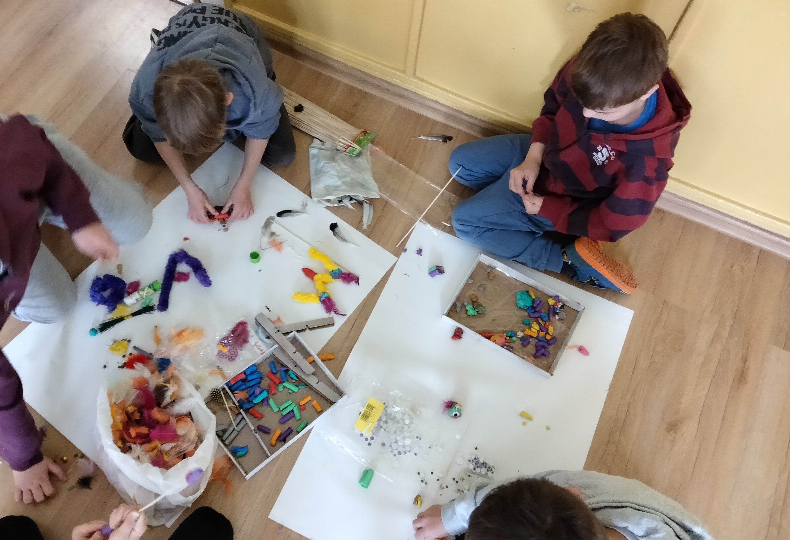 Grupa dzieci siedzi na podłodze i lepi drobne przedmioty z plasteliny.