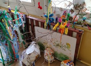 Instalacja artystyczna składająca się z gałęzi, kolorowej bibuły i dużych kartek pomalowanych farbami.