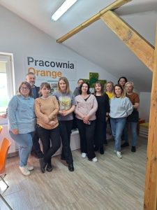 Grupa osób pozująca do zdjęcia w pomieszczeniu. W tle widać napis "Pracownia Orange".