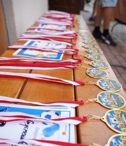 Medale ułożone na stole w rzędzie. Do medali przypięte są biało-czerwone tasiemki.
