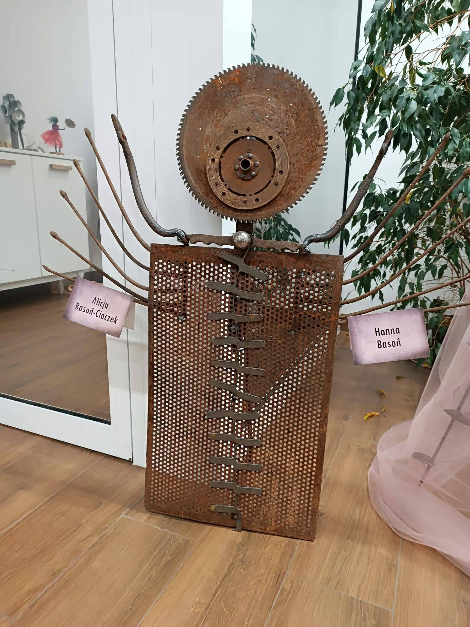 Zdjęcie przedstawia figurkę wykonaną z metalowych elementów, m.in. tarcz, siatki, wideł etc. Figura została skonstruowana na kształt ludzkiej sylwetki.