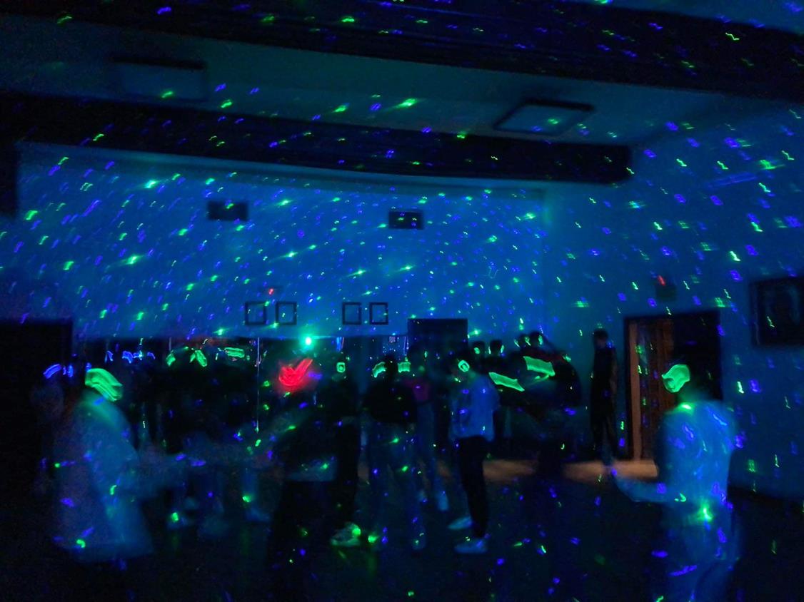 Na zdjęciu widać jedynie zarysy sylwetek tańczących ludzi. Półmrok przecinają lasery i światełka słuchawek Silent Disco.
