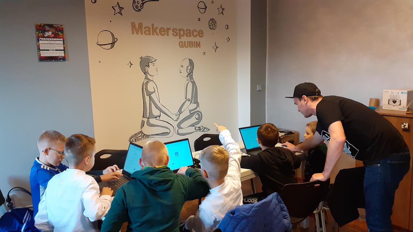 Sześciu młodych chłopaków siedzi przed komputerami. Ich mistrz Pan Konrad podpowiada jak dobrze projektować w 3D. W tle rysunek z napisem Makerspace Gubin.