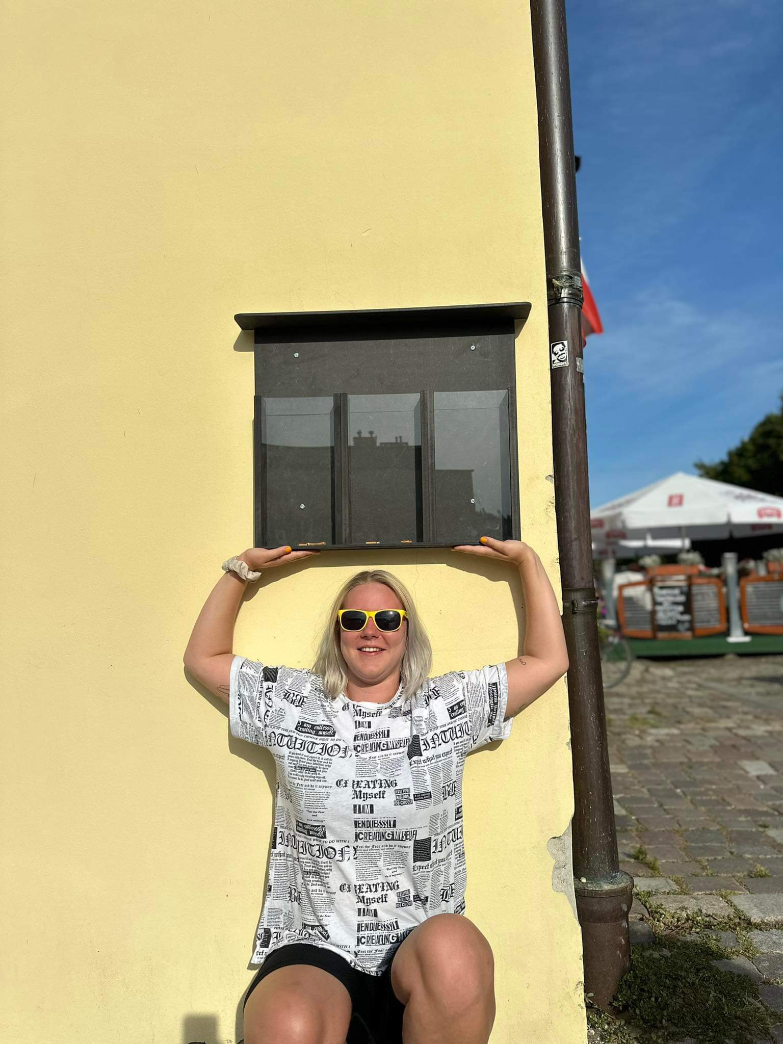 Ola w żółtych okularach pozuje na tle żółtej ściany i trzyma cos and głowa
