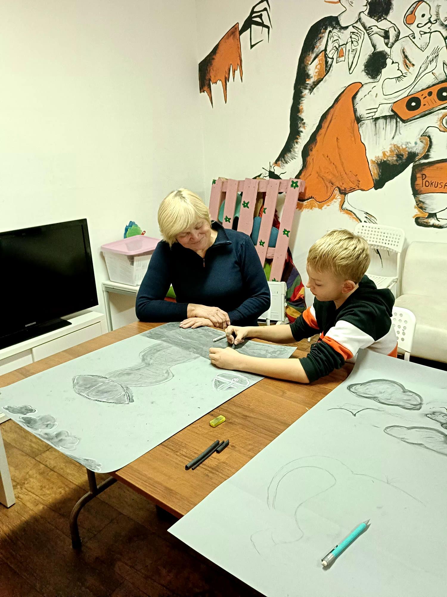 chłopiec i kobieta siedzą przy stole i malują obrazy węglem