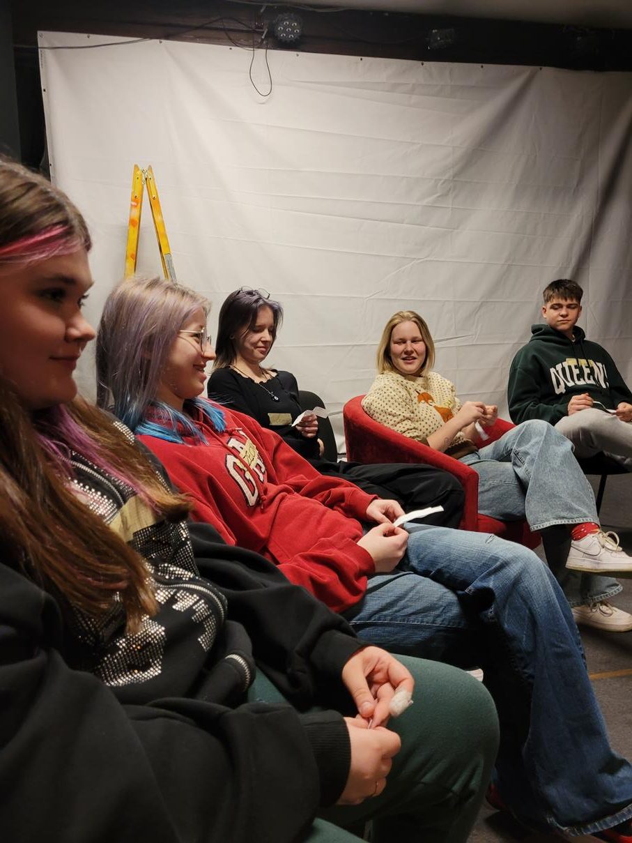 zdjęcie czwórki młodych osób, są uśmiechnięci, siedzą na krzesłach w tym jedna z dziewczyn na czerwonym fotelu