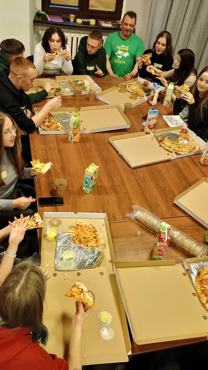 zdjęcie grupy młodych osób przy dużym stole, jedzą pizze