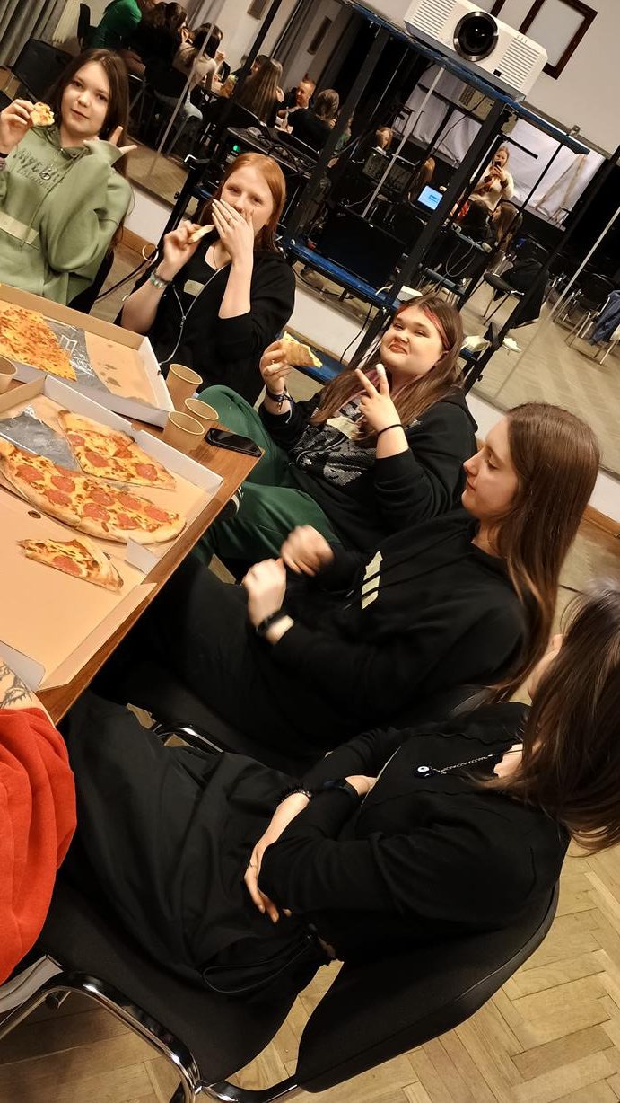 5 młodych dziewczyn, przy stole jedzą pizze