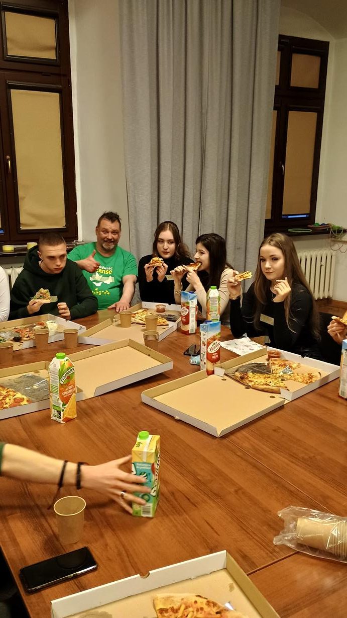 5 osób siedzących przy stole, jedzą pizze