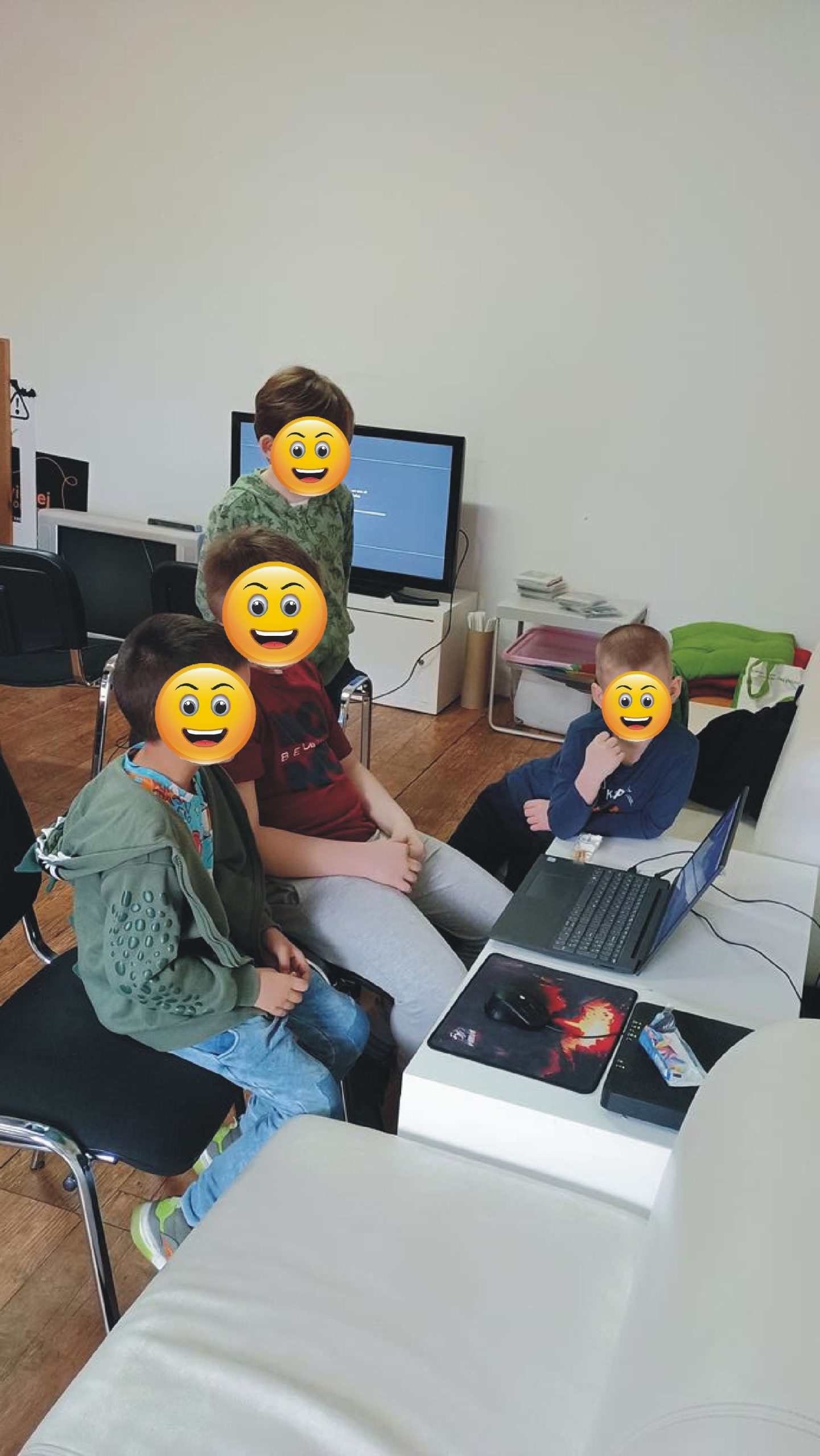 czterech chłopców ogląda cos na laptopie, maja pozasłaniane buzie emotkami
