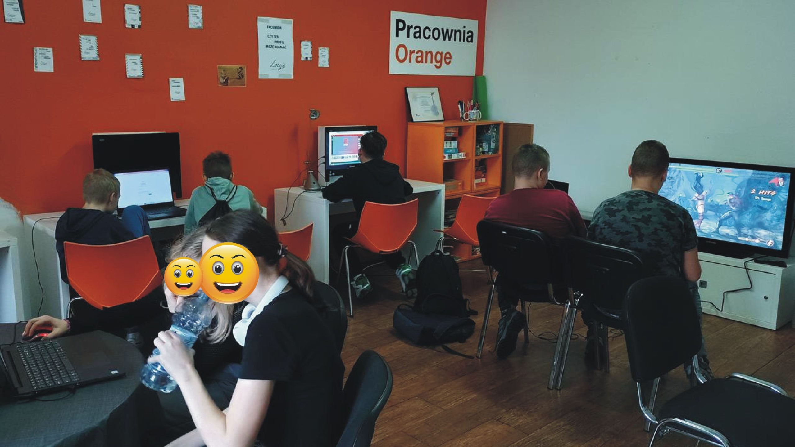zdjęcie z wnętrza pracowni orange, młodzi ludzie siedzą przy komputerach, dójka starszych chłopaków gra na playstation