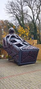 Na zdjęciu widać stary kontener na śmieci, którego obejmuje swoimi mackami wielka ośmiornica. Kontener przyozdobiony jest materiałem identycznym do tego, z którego zrobiona jest ośmiornica. Wszystkie materiały były śmieciem, który zamiast trafić na wysypisko, ozdabia teraz przestrzeń publiczną.