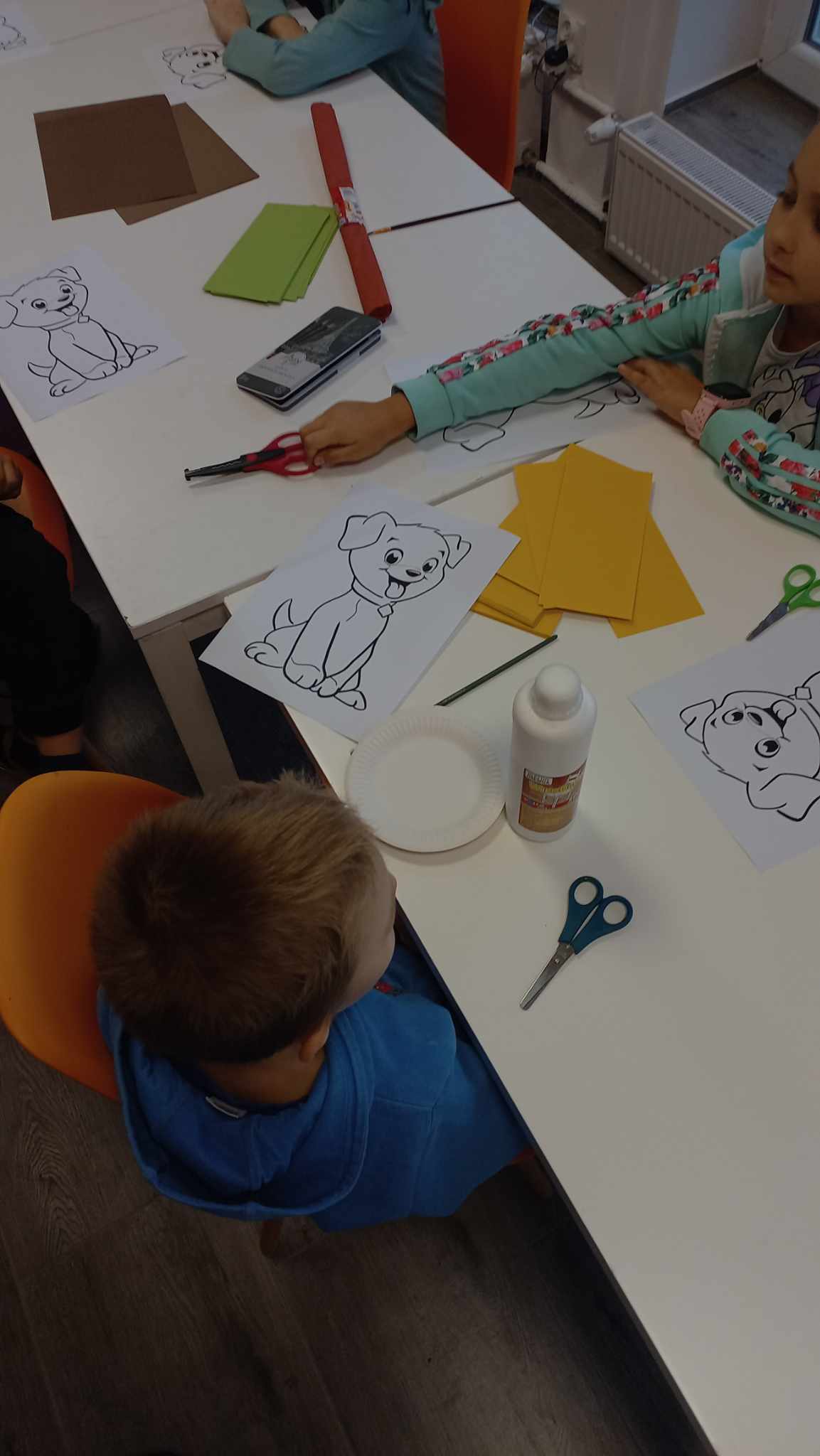 Dzieci siedzące wokół stołu przygotowujące się do tworzenia portretów psiaków