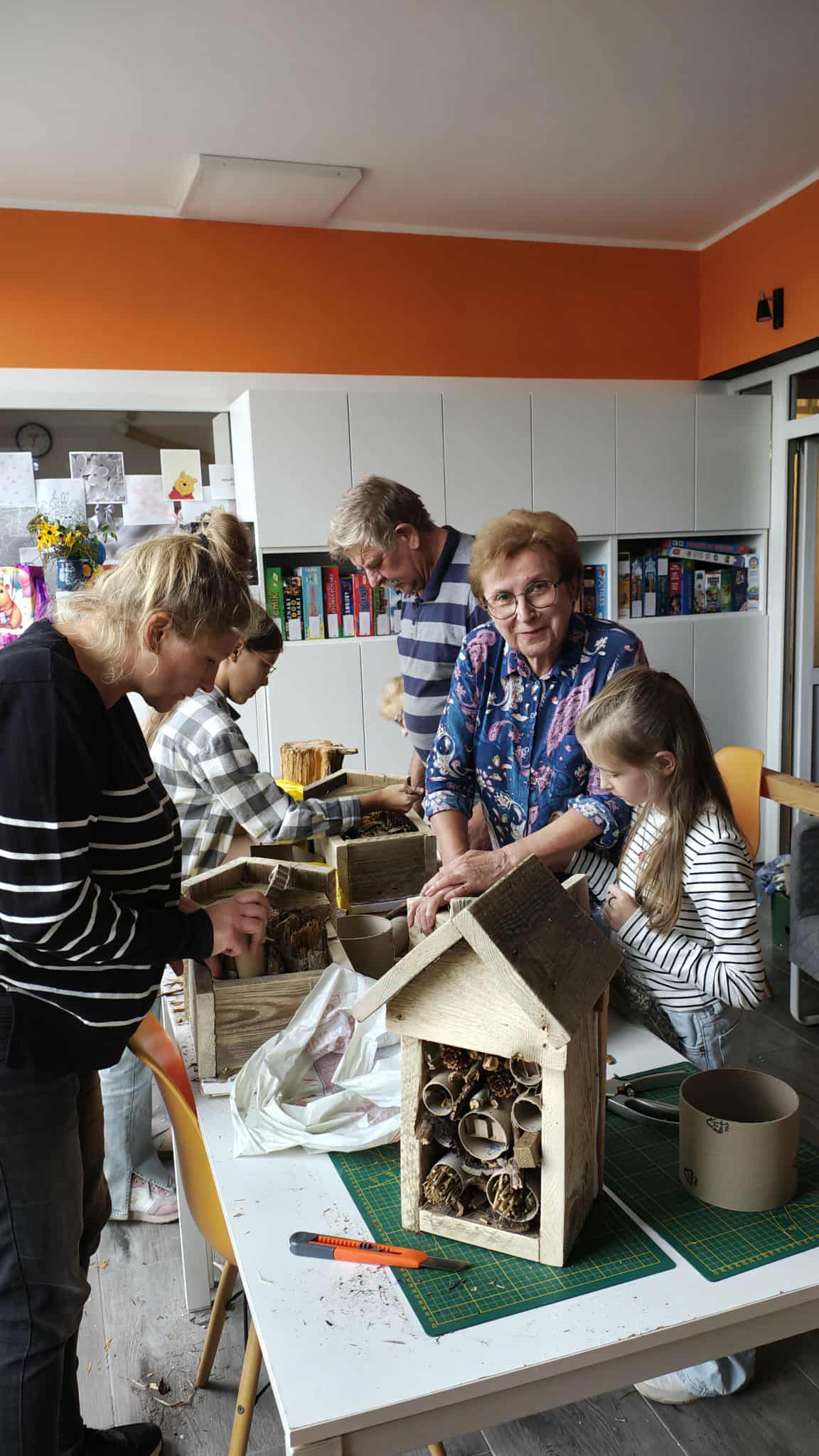 grupa osób przy stole warsztatowym pełnym drewnianych materiałów do domków