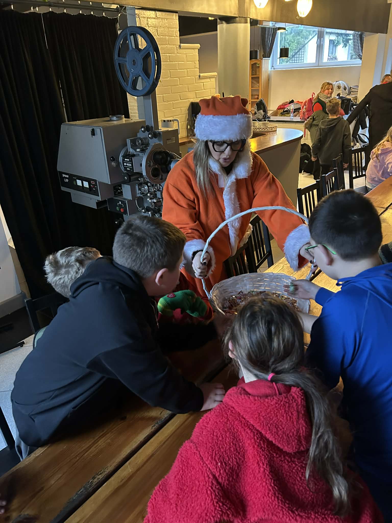 Kobieta w stroju św. Mikołaja rozdaje dzieciom prezenty.