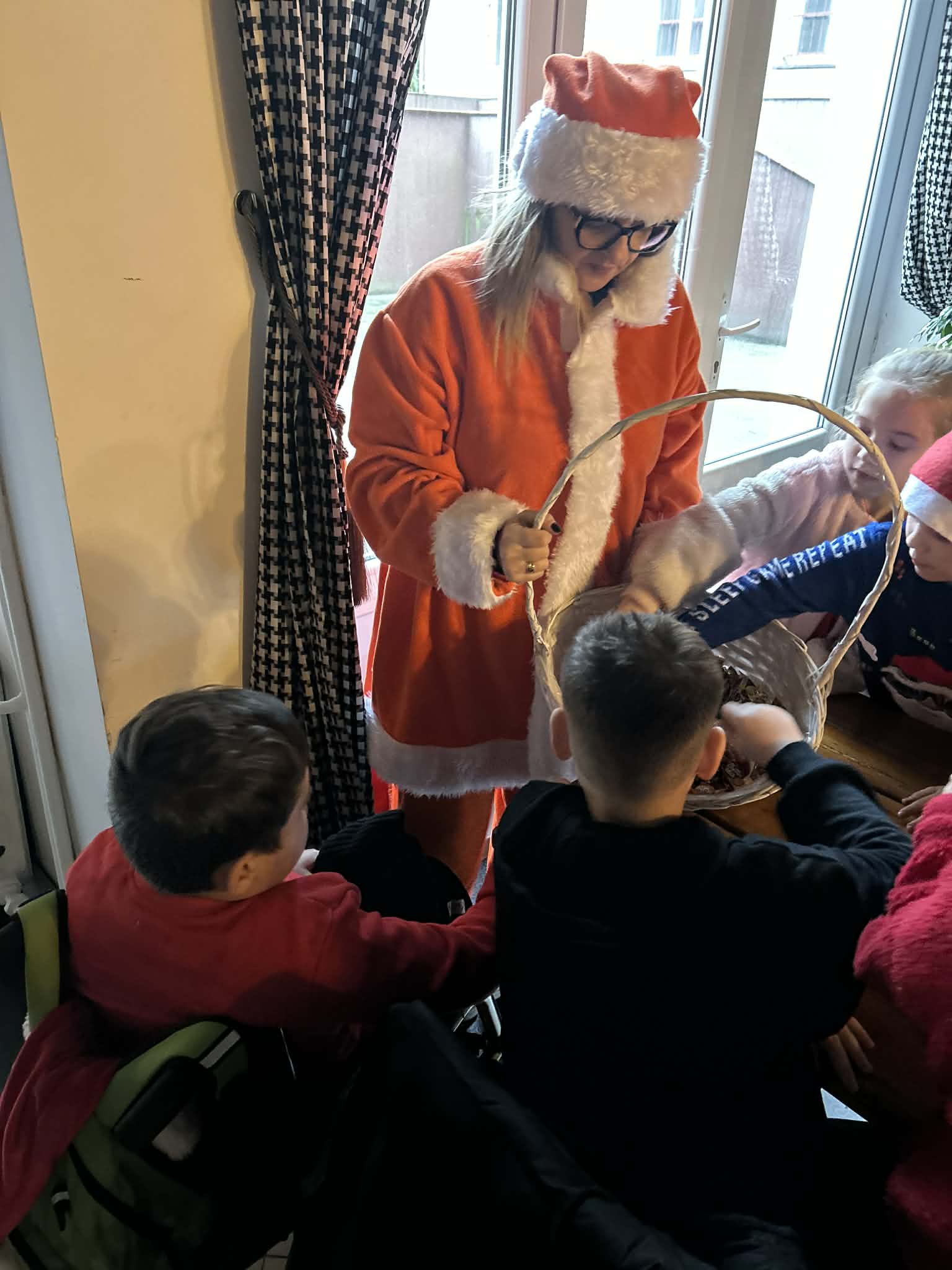 Kobieta w stroju św. Mikołaja rozdaje dzieciom prezenty.