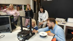 prowadzący opisuje kilku osobom budowę drukarki 3D