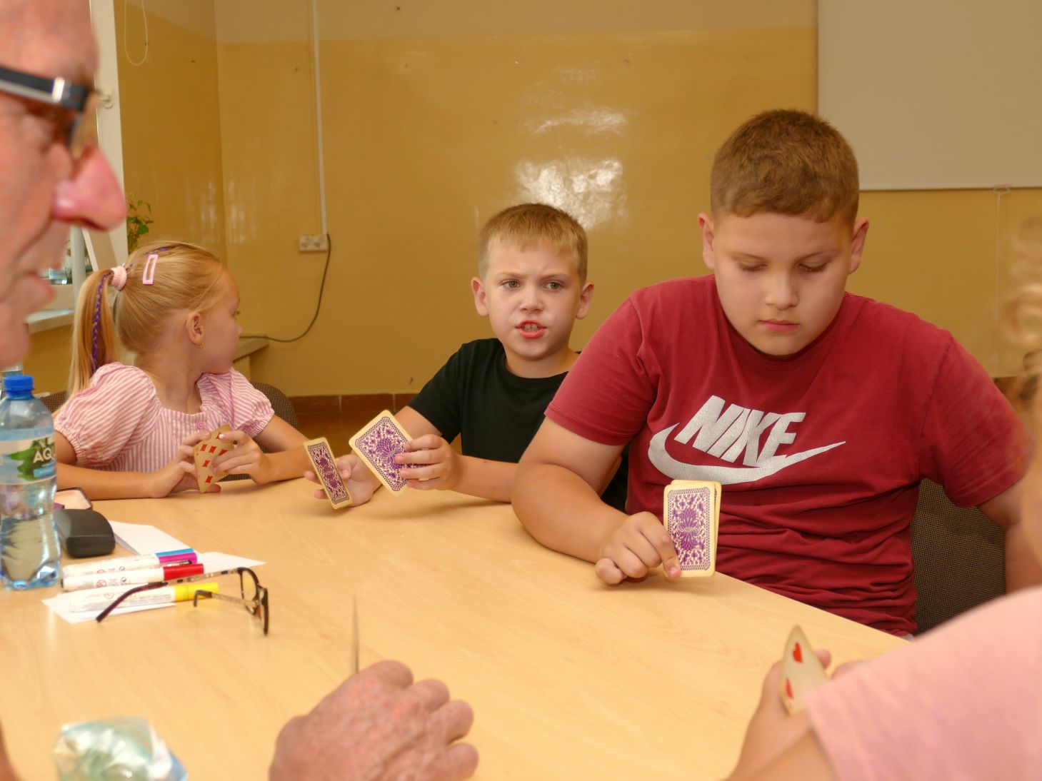 trójka dzieci przy stole trzymają w rękach karty do gry