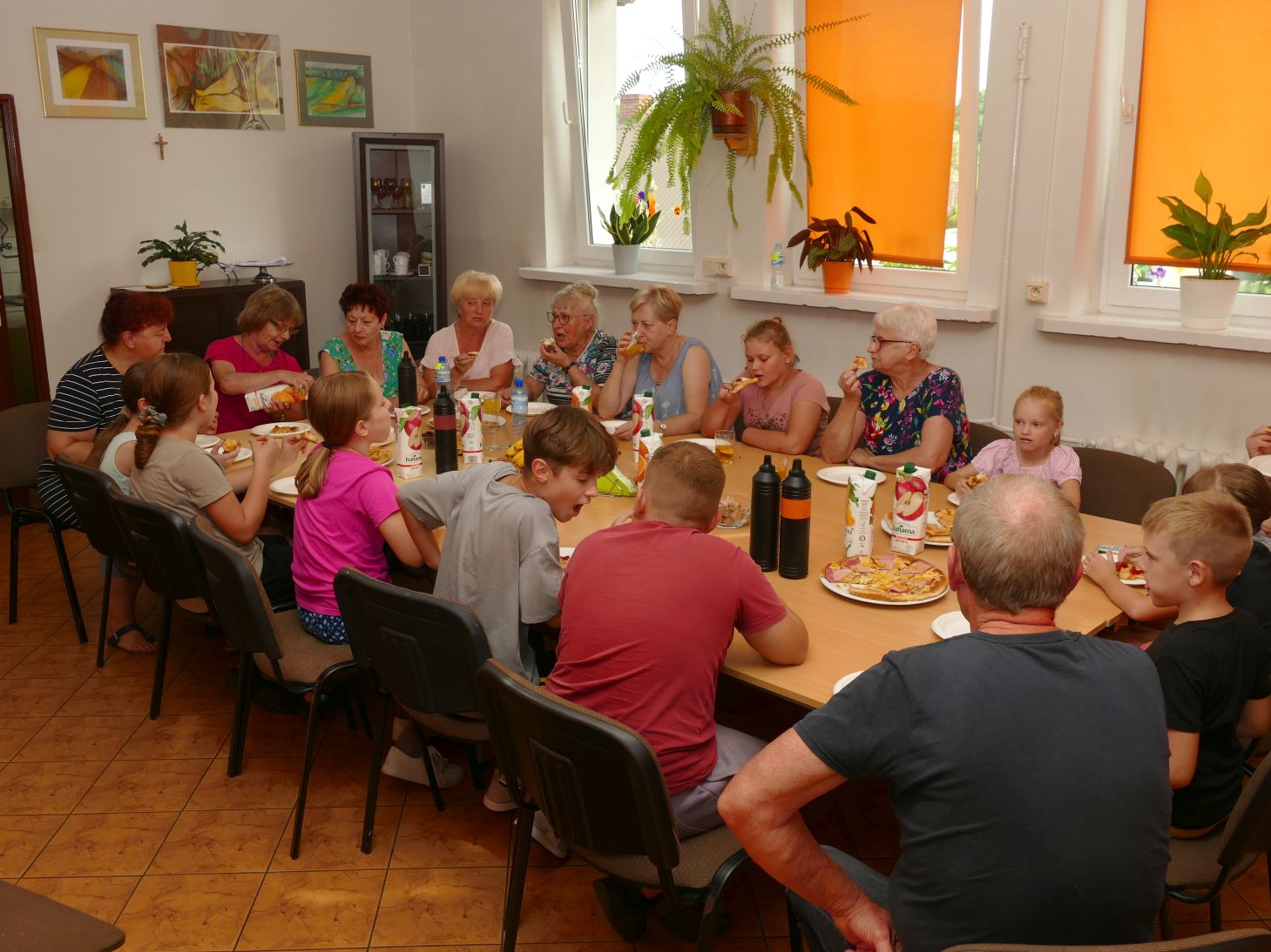 grupa młodych i starszych osób siedzi przy stole i wspólnie jedzą