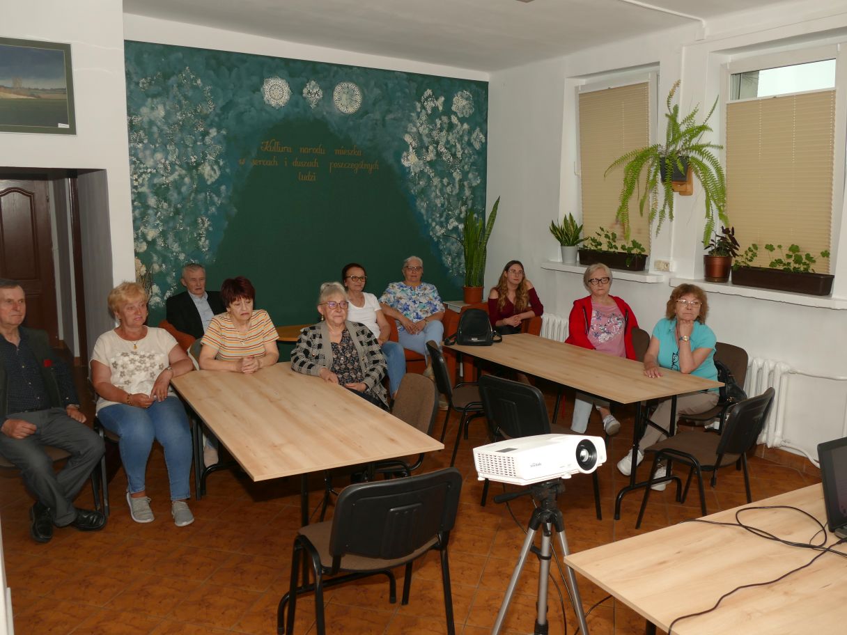 Grupa osób siedząca przy stole, skupiona na oglądaniu filmu instruktażowego