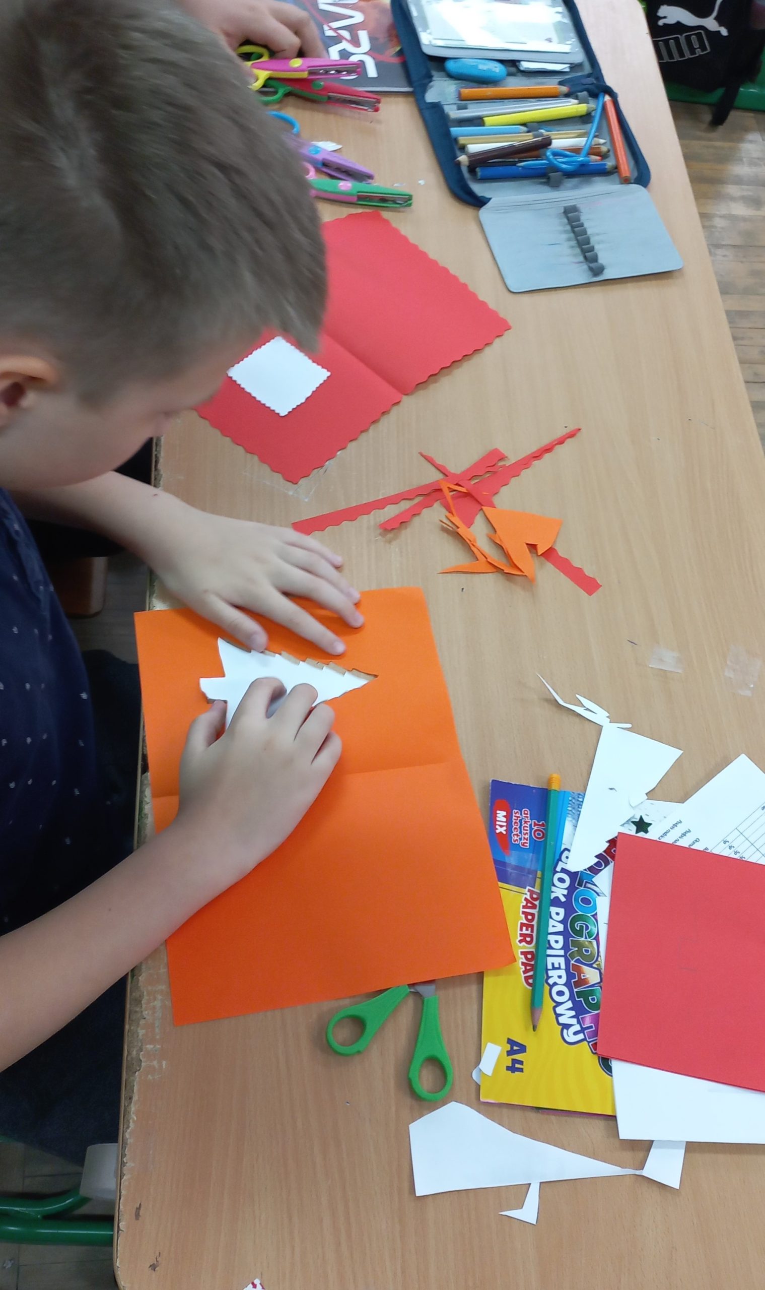 chłopiec robi kartkę na święta z pomarańczowego papieru