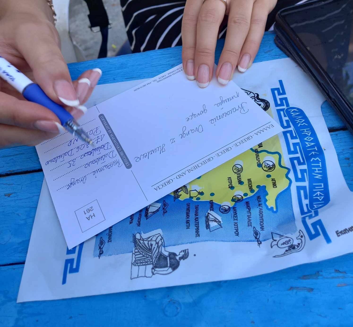 kobieta pisze pozdrowienia na pocztówce z Grecji