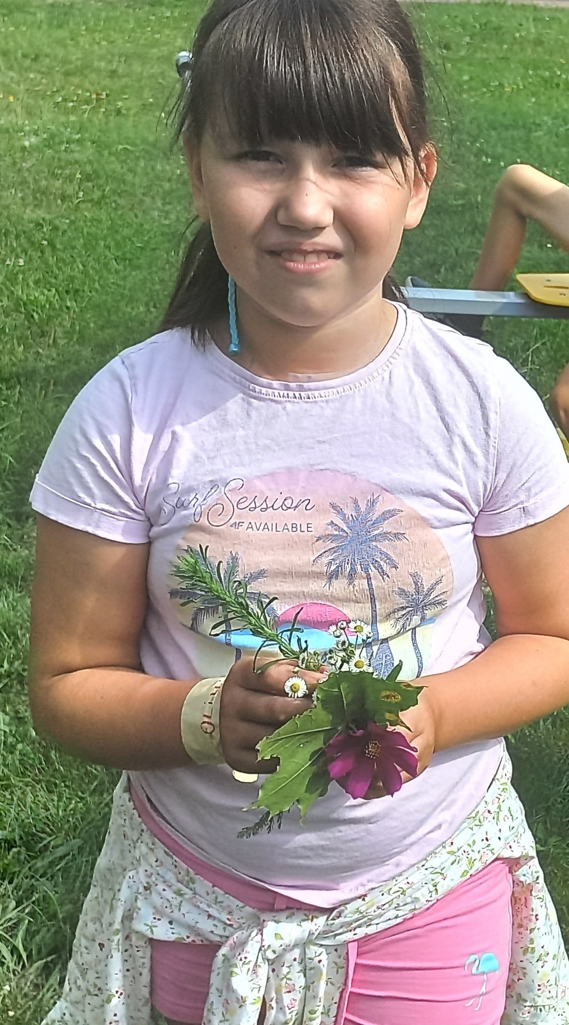 dziewczynka w jasno różowej bluzce trzyma w rękach kwiatki