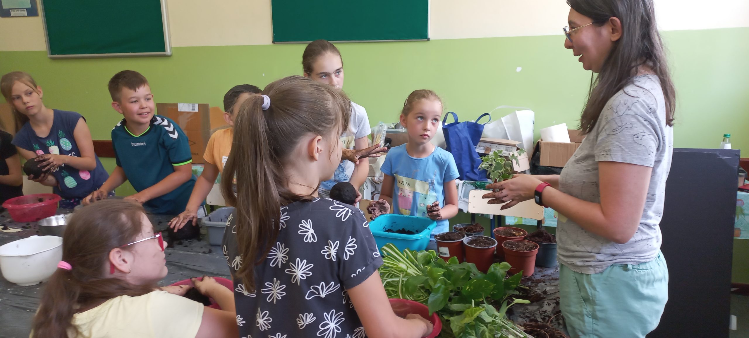 prowadząca stoi przy stole i tłumaczy dzieciom jak robić roślinne ozdoby