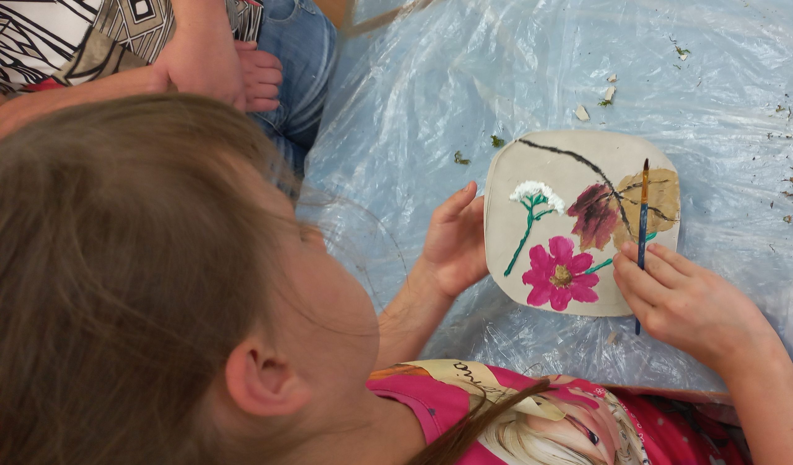 dziewczynka maluje gliniany obrazek na którym odbiła kwiatki
