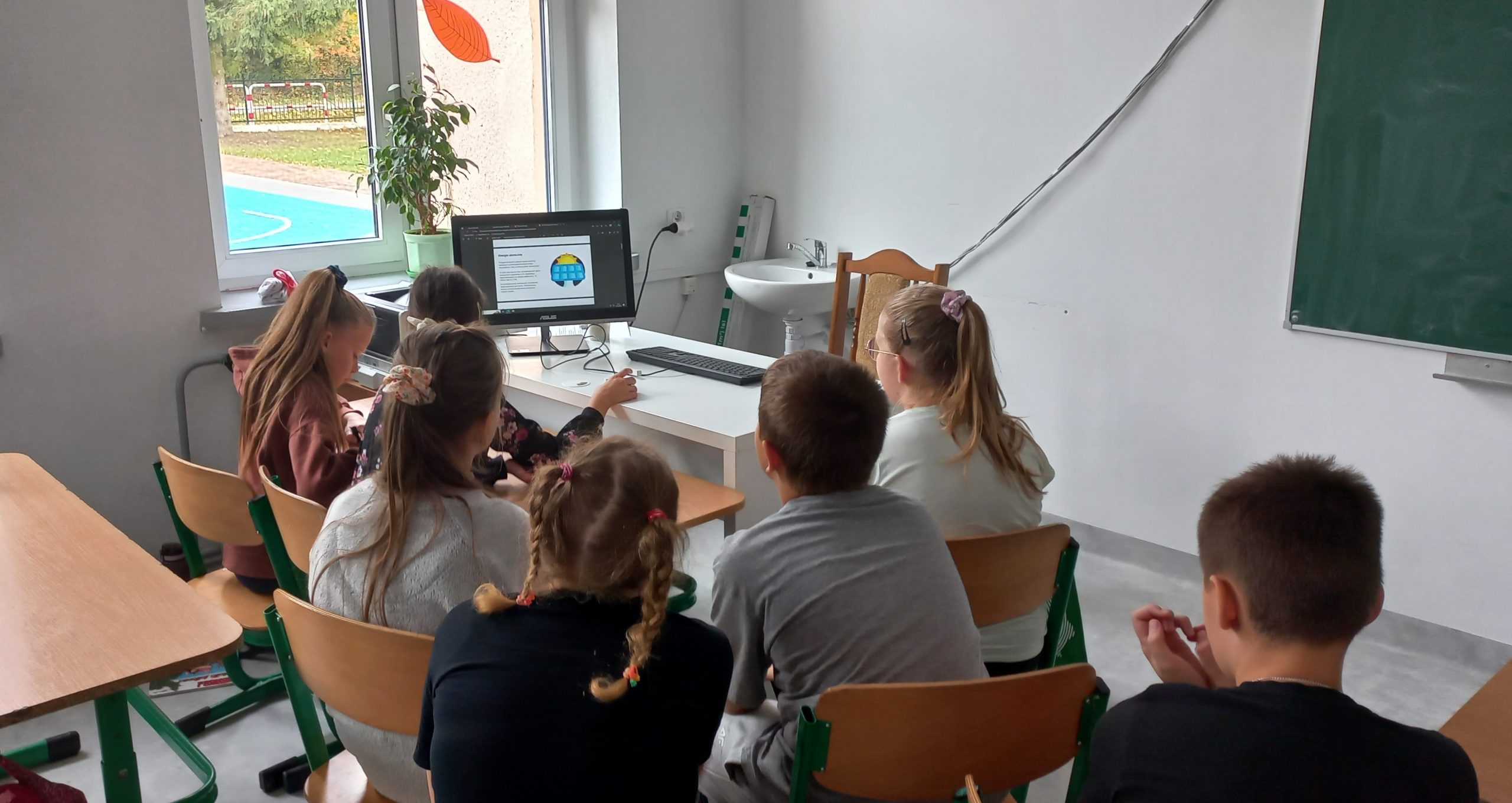 dzieci siedzące koło biurka oglądają prezentacje wyświetlaną na komputerze