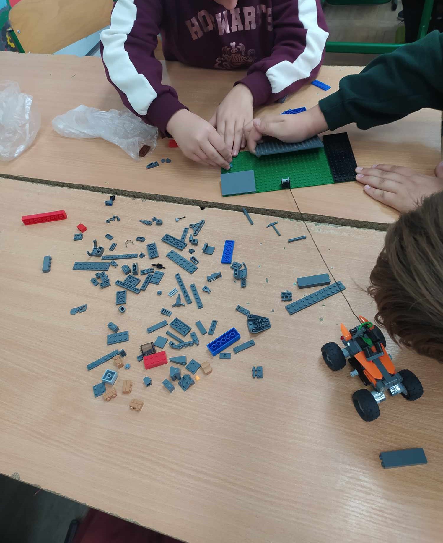 dzieci budują makietę z rozsypanych na stole klocków lego
